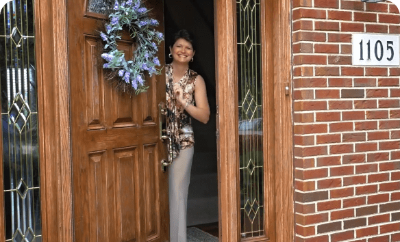 This photo shows a woman inside a home peering out the front door